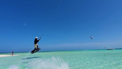 Man-sail-on-caribbean-sea-water-and-jump-doing-kitesurfing-tricks,-los-Roques