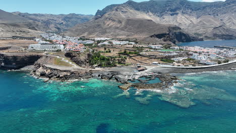 Fantastische-Luftaufnahme-Im-Orbit-Und-In-Mittlerer-Entfernung-Von-Der-Küste-Und-Wo-Sich-Die-Hotels-Und-Gebäude-An-Der-Küste-Des-Hafens-Von-Agaete-An-Einem-Sonnigen-Tag-Und-Auf-Der-Insel-Gran-Canaria-Befinden