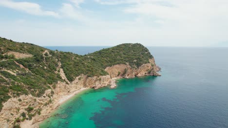 Rotating-Aerial-View-Over-A-Rocky-Seaside,-Turquoise-Water,-Lush-Vegetation,-Fari-Beach,-Thassos-Island,-Greece