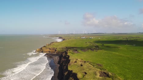 Drone-flyover-New-Zealand-coastal,-reveal-huge-wind-farm-on-horizon-at-Waipipi
