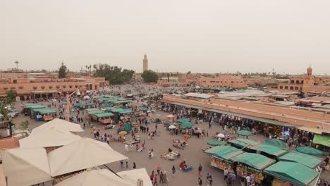 Looking-down-over-Jemaa-el-Fna-people-bustling-around-busy-scenic-marketplace-square,-Morocco