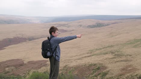 Young-boy-outdoors-standing-on-a-countryside-hill-top,-admiring-the-moorland-views