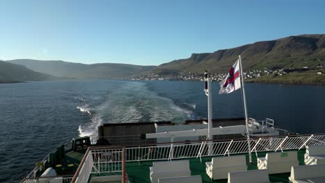 Wide-shot-of-waving-flag-on-Smyrill-ferry-and-tvororyi-island-in-background