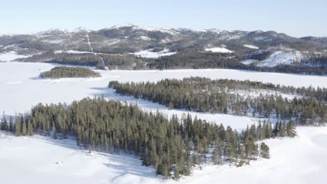 Aerial-View-Of-Snow-covered-Lake-With-Forest-And-Mountain-Views-In-Winter