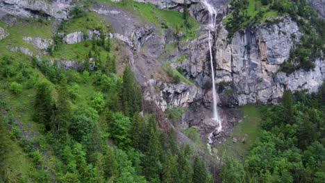 Aerial-Descending-Drone-view-of-Almenbachfall-waterfall-in-Kandertal-flowing-among-pine-trees-and-alpine-rocks,-Kandersteg-Berner-Oberland-Switzerland
