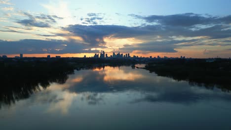 Drone-aerial-shot-of-Warsaw-skyline-at-sunset,-with-the-city's-skyscrapers-reflecting-on-the-calm-waters-below