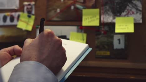 In-front-of-the-evidence-board,-the-detective-captures-important-details-by-taking-notes-in-a-notebook