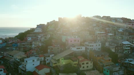 Aerial-view-circling-dense-Favela-in-Arraial-do-Cabo-mountain-neighbourhood-with-sunlight-behind-summit,-Rio-de-Janeiro