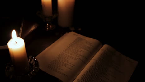 Above-Shot-of-Holy-Bible-Lit-by-Candle-Light-in-a-Hidden,-Dark-Place