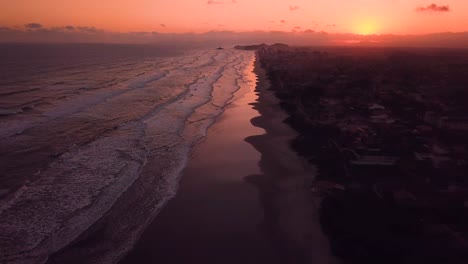 Tilting-aerial-shot-of-beach-in-sunset,-beautiful-sky-and-waves