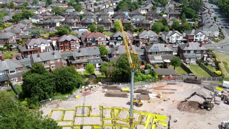 Tall-crane-setting-building-foundation-in-British-town-neighbourhood-aerial-view-rising-over-top