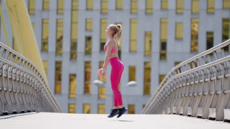 Young-fit-woman-in-pink-sportswear-works-out-on-bridge,-wide-side-view