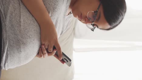 Brunette-pregnant-woman-with-glasses-sitting-typing-on-a-mobile-phone