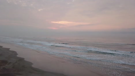 Slow-flying-over-the-Atlantc-ocean-beach-in-Brazil-in-early-pink-sunrise,-aerial-shot