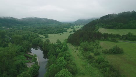 Die-Luftaufnahme-Zeigt-Eine-Malerische-Neblige-Hügellandschaft-Mit-Einem-Sich-Schlängelnden-Fluss,-Der-Durch-Ein-üppiges-Tal-Fließt