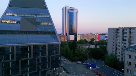 Aerial-view-of-modern-offices-in-Warsaw-with-the-setting-sun-casting-reflections,-alongside-buildings-from-the-80s