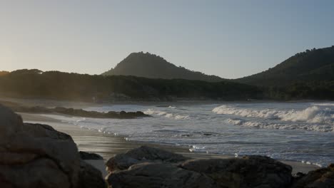 Ocean-Waves-coming-creeping-onto-beach-at-sunset-with-mountains-in-the-background