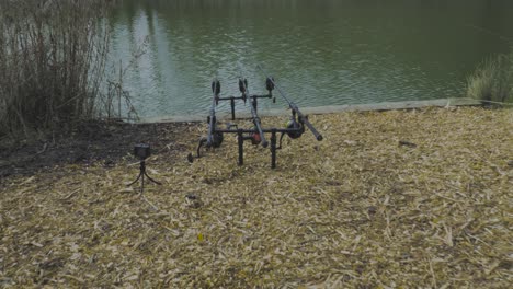 Zoom-in-shot-over-carp-fishing-rods-and-bite-alarms-setup-in-the-lake-water-in-Norfolk,-England-on-a-sunny-day