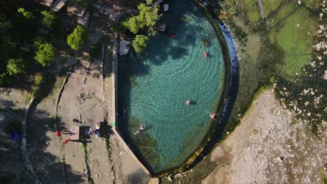 Drone-looking-straight-down-with-some-people-enjoying-the-water-at-the-turquoise-water-of-the-Benja-thermal-pool-in-Permet,-Albania