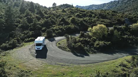 Camping-Van-Makes-a-U-Turn-up-the-Green-Hills,-Wild-Roads-in-South-of-France,-Caravan-Car,-Aerial-Drone-Landscape-Shot