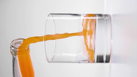 Vertikale-Zeitlupenaufnahme-Von-Karottensaft,-Der-Vor-Weißem-Hintergrund-In-Ein-Leeres-Glas-Gegossen-Wird