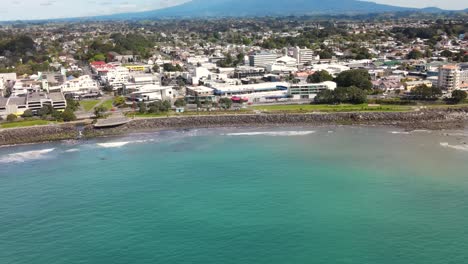 Aerial-flyover-New-Zealand-coastal-city-of-New-Plymouth,-tilt-up-reveal-Taranaki-volcano-on-horizon