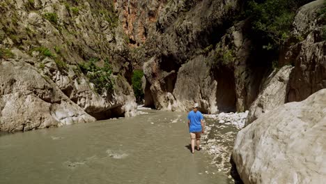Brave-woman-walks-in-rapid-flowing-gorge-river-with-steep-ravine-cliffs