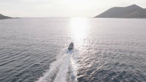 Aerial-orbiting-shot-of-motorboat-speeding-on-Mediterranean-Sea-against-golden-sunlight-at-sunset-in-Greece,-cinematic