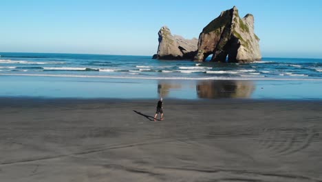 Man-running-on-sandy-beach-enjoying-summer-sunny-day-at-Wharariki-Beach,-New-Zealand