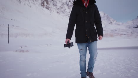 Man-holding-digital-video-camera-walks-in-snow,-travel-in-nature-with-modern-technology