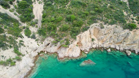 Top-Down-View-Of-A-Rocky-Shoreline-With-Turquoise-Water,-Lush-Vegetation,-Fari-Beach,-Thassos-Island,-Greece