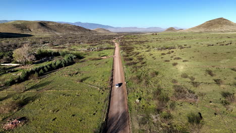 Aerial-shot-of-car-on-dirt-road-in-Willcox,-Arizona,-wide-tracking-drone-shot-with-mountains-in-the-background-with-dust-trails