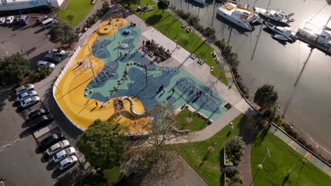 Wunderschöne-Drohnenaufnahme-Eines-Spielplatzes-Und-Eines-Stadtparks-Am-Flussufer
