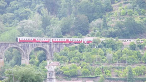 Amplia-Vista-De-Un-Tren-Rojo-Sobre-Un-Puente-Histórico-En-El-Valle-Del-Río-Douro,-Portugal-En-Verano