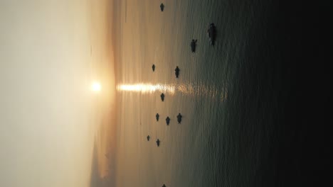 Vertical-shot-of-a-Bali-sunrise,-aerial-drone-shot-of-the-sun-rising,-reflection-in-a-calm-sea,-boats-floating-in-the-ocean