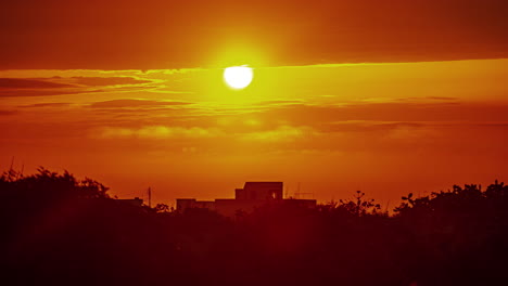 Bright-red-ball-of-sun-rises-like-fire-above-concrete-tropical-building,-timelapse