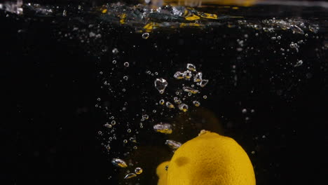 Viele-Frische-Zitronen-In-Zeitlupe-Fallen-Mit-Blasen-Ins-Wasser