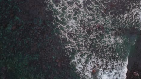 Top-down-aerial-of-waves-crashing-on-shallow-water,-red-and-blue-seabed