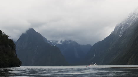 A-ship-appears-small-surrounded-by-towering-cliffs-and-waterfalls-showcases-the-breathtaking-beauty-of-Milford-Sound-in-New-Zealand