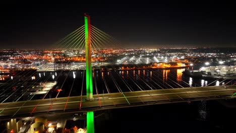 Night-aerial-of-Gerald-Desmond-Bridge-over-the-city-lights-of-Long-Beach,-CA