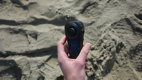 Mann-Stellt-360-Grad-Kamera-Im-Sand-Eines-Strandes-Auf