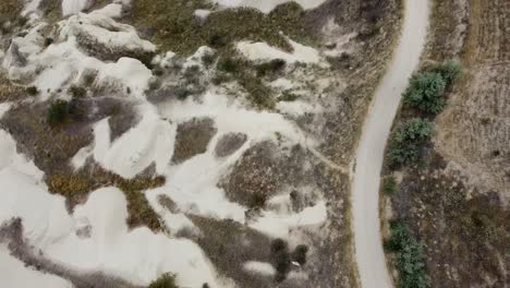 Aerial-view-of-a-drone-following-a-dirt-track-through-the-green,-rocky-landscape-of-Cappadocia-in-Turkey
