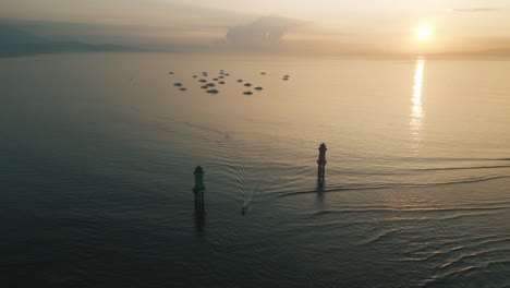Bali-sunrise-drone-aerial-shot,-sun-rising-above-a-calm-sea,-floating-boats-on-the-ocean-and-waves-are-serene