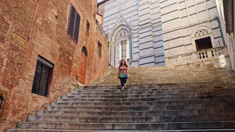 A-young-lady-walks-down-the-steps-leading-from-the-medieval-Siena-Cathedral,-Siena,-Italy