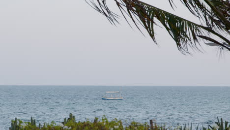 Small-fishing-boat-at-sea-in-distance-with-beach-foreground-in-Africa