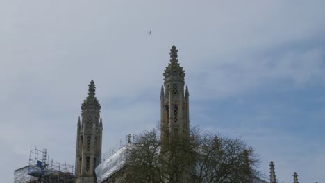 Plane-soars-through-blue-sky-with-gothic-cathedral-in-Cambridge-England