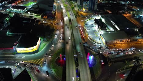 A-stunning-aerial-drone-view-of-the-night-traffic-at-San-Pedro-Highway,-Costa-Rica,-forward-movement,-camera-looking-down-over-a-roundabout