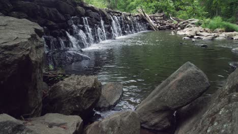 Pan-up-towards-water-rushing-through-stacked-rocks-making-a-dam-in-creek