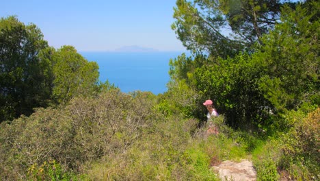Shot-of-a-woman-hiking-along-rugged-terrain-surrounded-by-lush-green-vegetation-in-Capri-Island,-Campania,-Italy-on-a-sunny-day