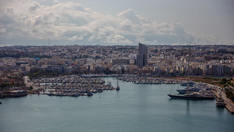The-city-of-Valletta,-Malta-and-the-harbor-with-many-boats-docked---cloudscape-time-lapse